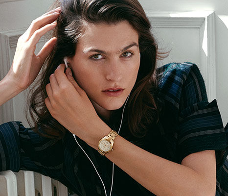 Woman in a dark striped outfit wearing a gold Vivienne Westwood watch.